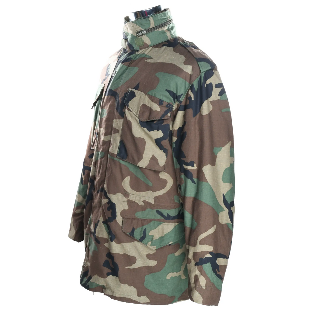 Angled front and side view of US Army M65 field jacket in woodland camo with flap pockets and stand collar.